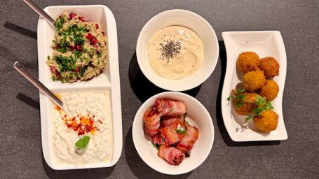 Vier Schalen mit verschiedenen Dips, gefüllten Bällchen und gefülltem Speck.